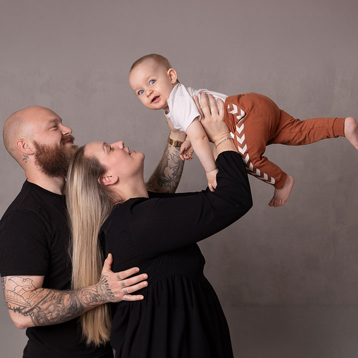 Familie på 3 smiler. Baby kigger på kamera